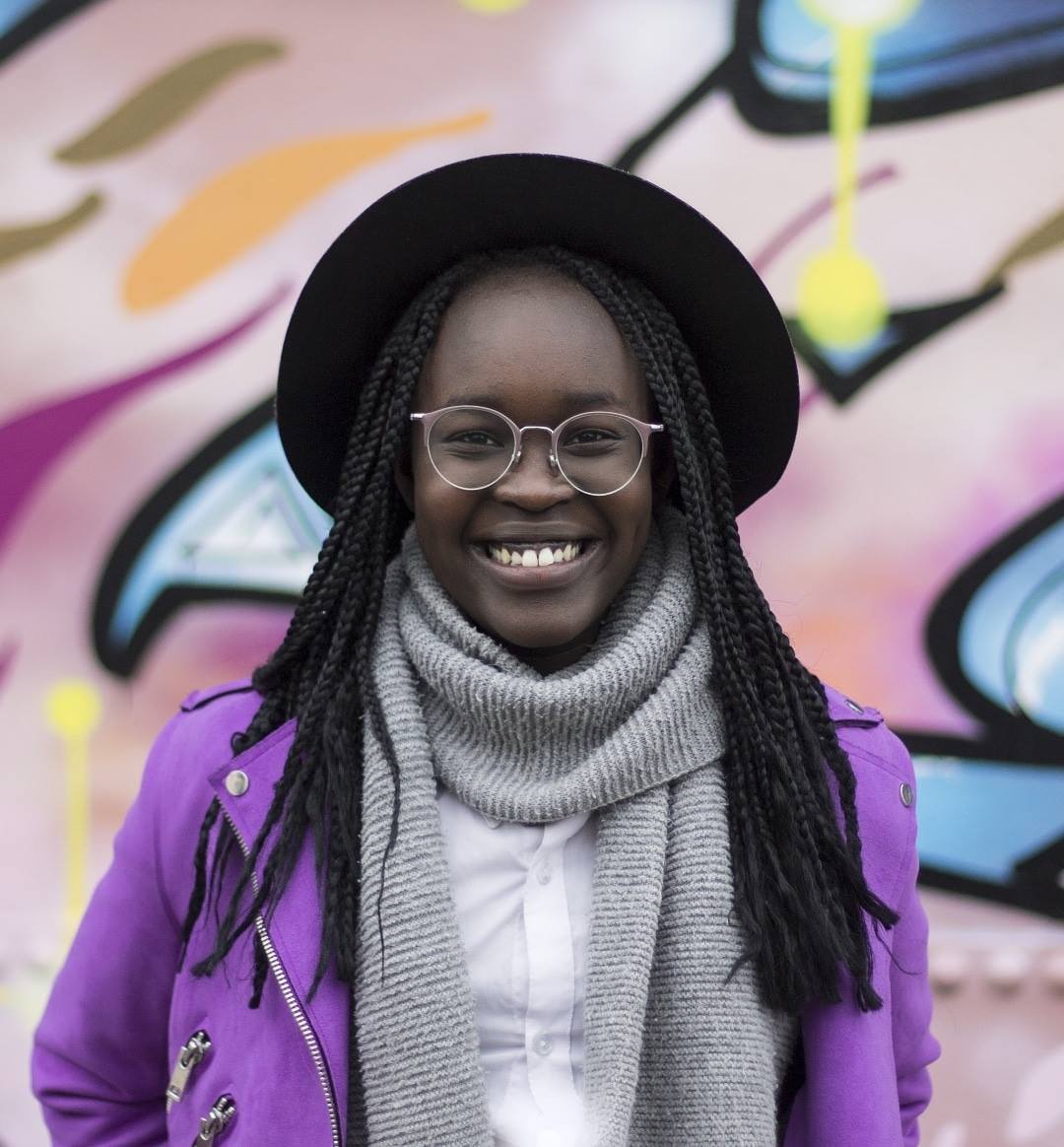 Ajak Majok seisoo graffittiseinän edessä ja hymyilee